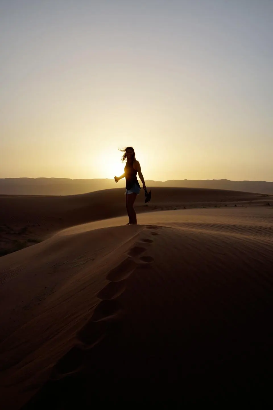 Silhouette d'une femme qui marche seule dans les dunes, face au soleil levant