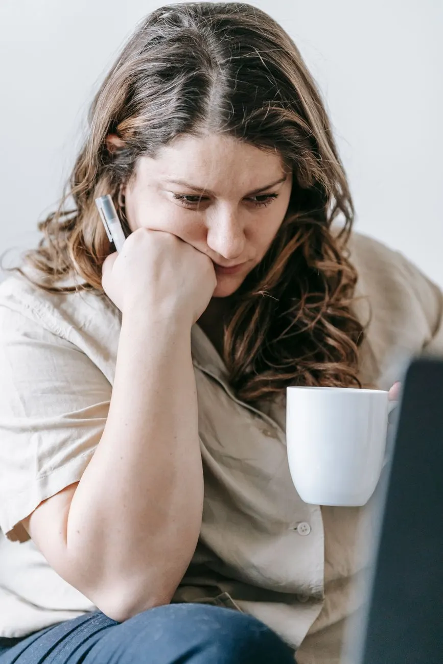 Femme pensive à son bureau, une tasse à la main, le regard perdu dans ses pensées