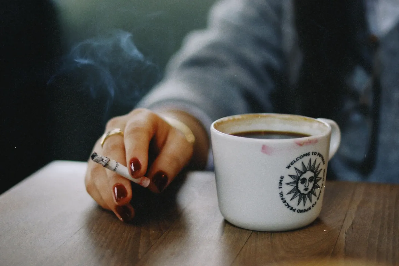Main tenant une cigarette posée à côté d'une tasse de café