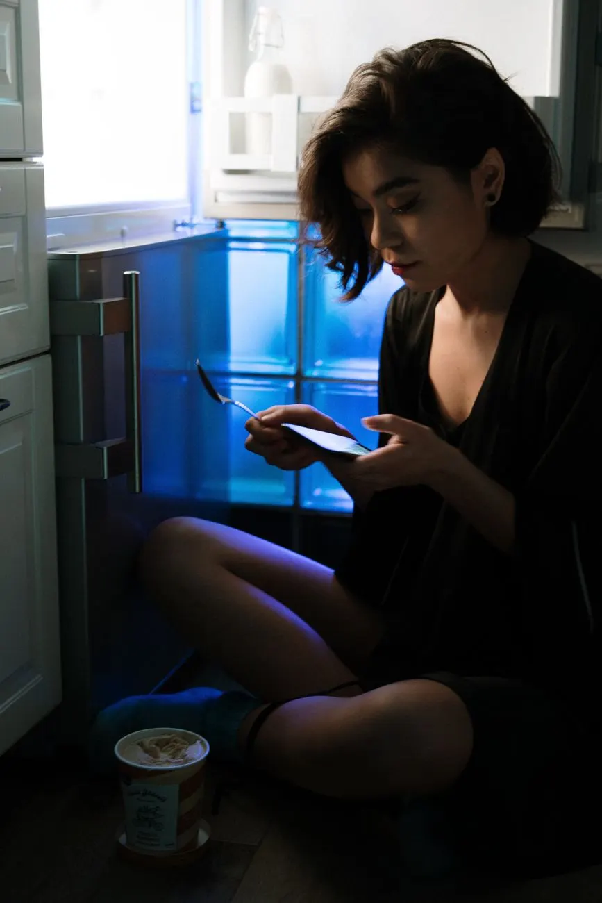 Femme assise le soir devant le réfrigérateur ouvert, en train de grignoter