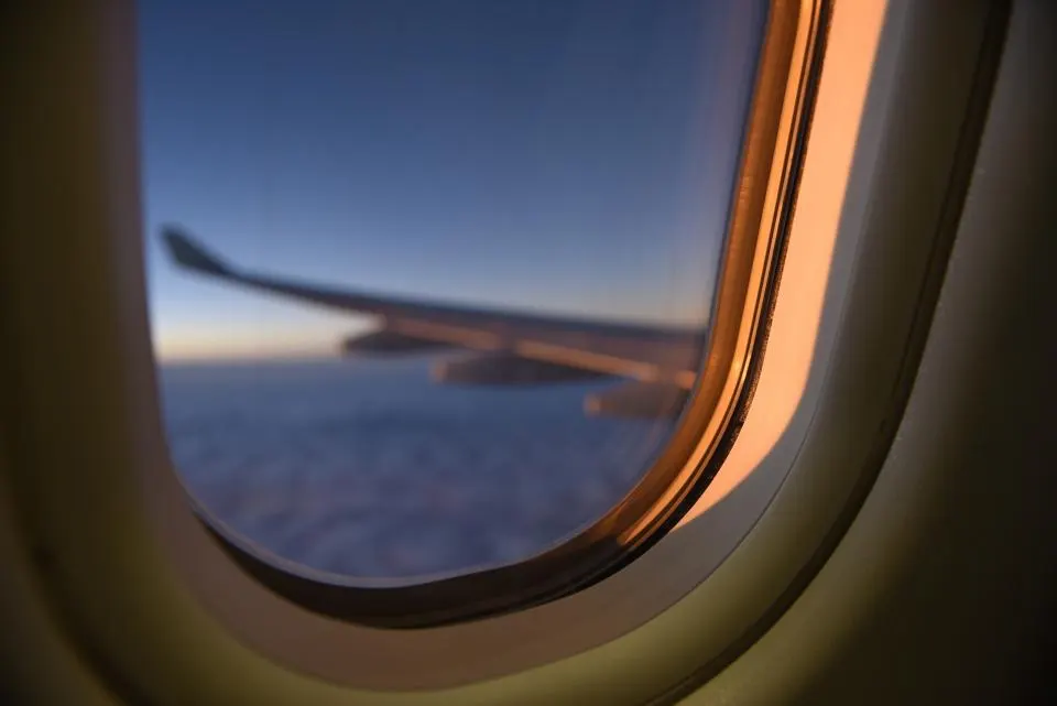 Vue par le hublot d'un avion : l'aile au-dessus des nuages, au coucher du soleil
