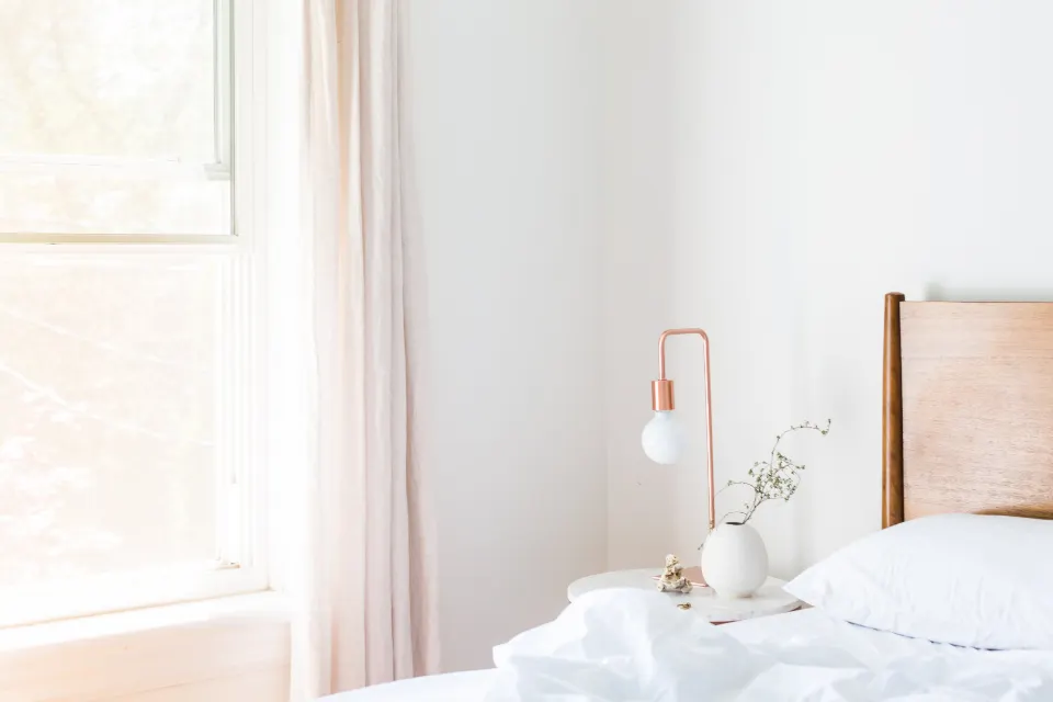 Chambre claire et épurée, lit fait près d'une fenêtre aux rideaux légers